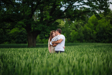 Loving parents embracing newborn infant, cuddling together near sprawling tree within lush green meadow landscape