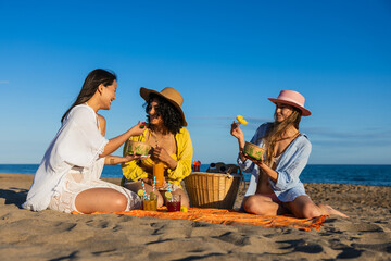 Multiethnic girls enjoying tropical fruits at beach picnic