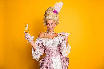 Elegant woman in retro costume with noble style holding glass of champagne against yellow background
