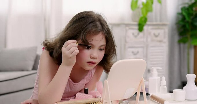 Young girl applying mascara in front of tabletop mirror, surrounded by makeup products. Scene highlights curiosity, self-expression, and exploration of beauty routines in a bright room.