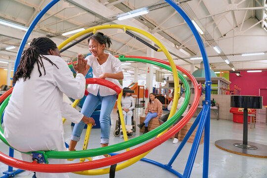 Instructor giving high five to teenager on gyroscope in science center