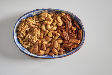 Assorted nuts in a stoneware container with a straw basket, on a white background. Almonds, Walnuts, Cashews and Chestnuts