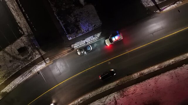 Top View Of The City At Night As A Police Car Halts Traffic. The Officer Steps Out, Approaching The Suspect In A Cinematic, Action-Packed Moment Within An Industrial Urban Area.