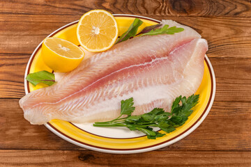 Pangasius fillet on yellow dish with lemon on rustic table