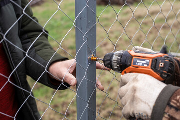 Workers install a chain-link fence in a garden, using a screwdriver to attach screws