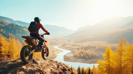 Fototapeta premium Extreme Rider climbing sand mountain top on off-road cross enduro motorcycle. Beautiful mountains landscape down on background, colourful autumn forest and river in sunshine.