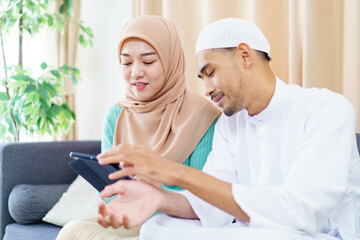 Obraz premium Good looking Asian muslim spouse reading and studying the Holy Koran together in living room.