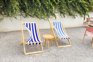 Blue white striped wooden deck chair on pebble sea shore or back yard garden, outdoor beach furniture, relax lounge calm patio place with seats, summer vacation, travel.
