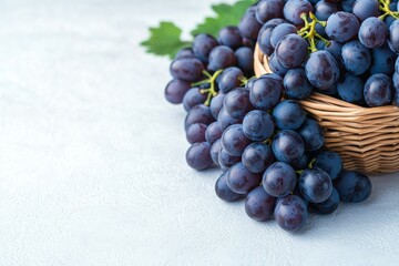 A basket filled with fresh purple grapes, accompanied by green leaves, set against a soft, light background.
