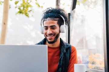 Smiling young man with headphones working on laptop in cafe
