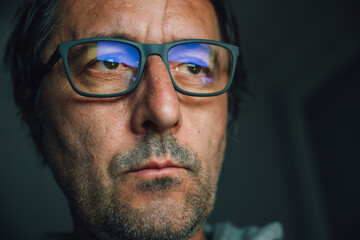 Concerned man with low vision wearing eyeglasses and looking at computer screen late at night