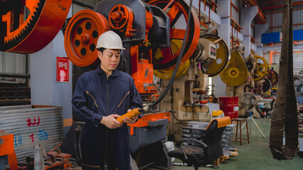 Naklejka premium Smart Japanese male mechanical engineer is using a remote control to operate a crane or robot in a metal sheet factory. Female expert technical worker is using remote controller to control machine.