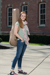 Fototapeta premium Beautiful young redhead woman on campus carrying a guitar case - smiling