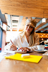 Latin influencer writing on notebook and teleworking in cafe