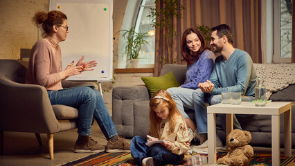 Psychologist lively talking and discussing problems of family. Parents sitting on couch with...