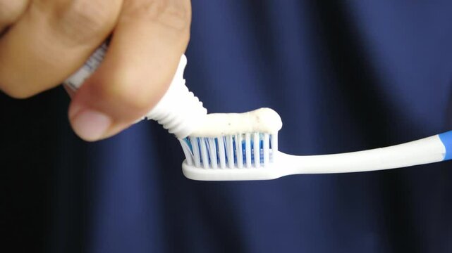 A hand pours toothpaste onto a toothbrush.