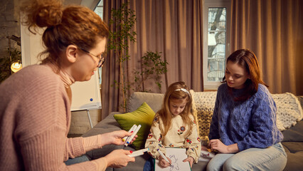 Psychologist and mother using art technique in communication with child, little girl drawing and...