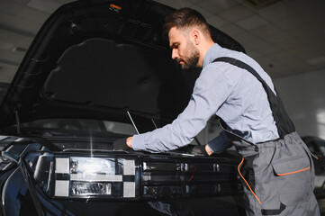 Mechanic Uses a Computer with an Augmented Reality Diagnostics Software. Specialist Inspecting Car's Engine to Quickly Spot Broken Components. Premium Car Service