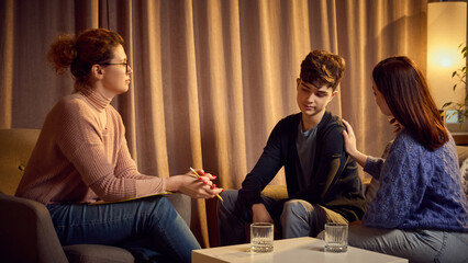Psychologist attentively listens to teenage boy and his mother during a family therapy session,...