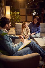 Happy mother and her little daughter sitting on sofa during their therapy session with psychologist...