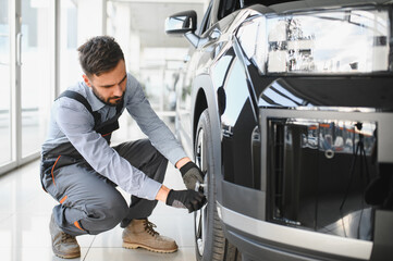 Car mechanic working in garage and changing wheel alloy tire. Repair or maintenance auto service....