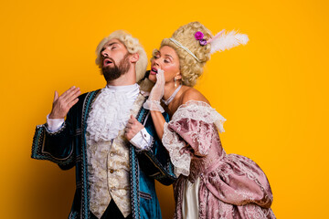 Elegant couple dressed in royal 18th-century costumes posing against a vibrant yellow background