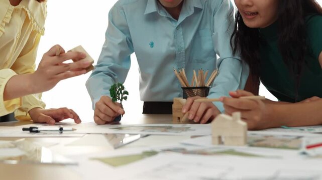 Architect and safety engineer discuss about position of tree use blueprint, model on table with architectural document, measurement tool and wooden block scatter around at modern office. Delineation.