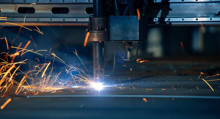 Plasma cutting machine cuts metal material with sparks, industrial background