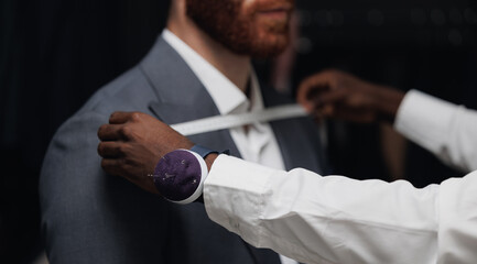 Professional tailor measuring customer for bespoke suit in luxury designer atelier