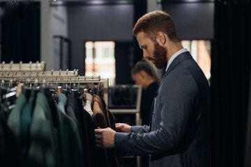 Portrait handsome client man in menswear store chooses suit. Luxury designer atelier shop