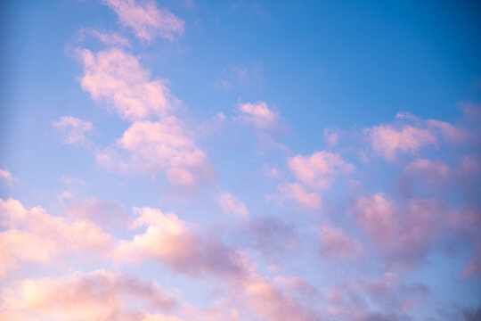 Scattered pink clouds drifting across a vibrant blue sky create a stunning sunset scene, radiating tranquility and warmth while inviting a sense of peacefulness and serenity