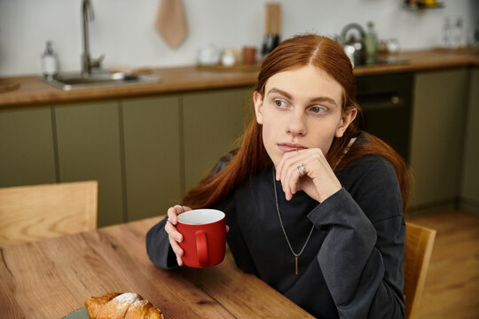 A young man with long hair enjoys a quiet moment in his stylish apartment, sipping coffee. - Powered by Adobe