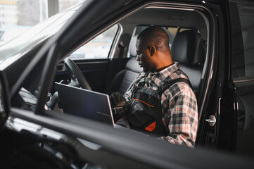 Black auto mechanic running diagnostic on laptop while analyzing engine problems in a workshop