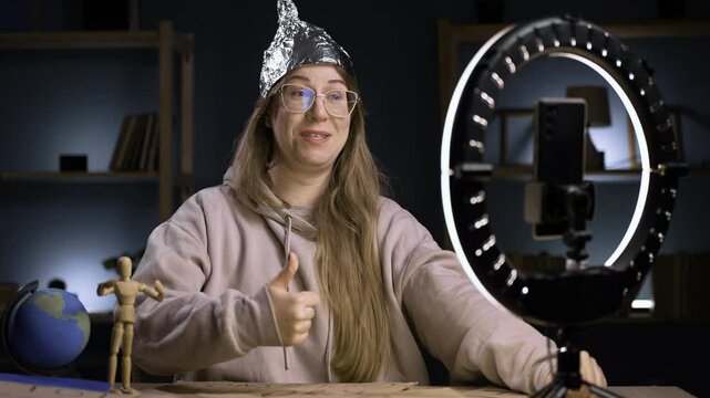 Strange crazy vlogger with cellphone, paranoid woman streaming at home conspiracy theory broadcasting in vlog, showing thumb-up likes gesture. blogging and conspiracy theory
