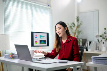 A woman is sitting at a desk with a laptop and a monitor