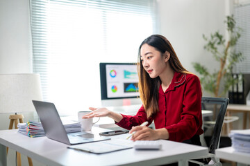 A woman in a red shirt is sitting at a desk with a laptop and a keyboard