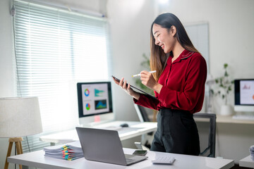 A woman in a red shirt is sitting at a desk with a laptop and a tablet