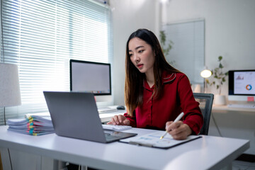 A woman is sitting at a desk with a laptop and a pen
