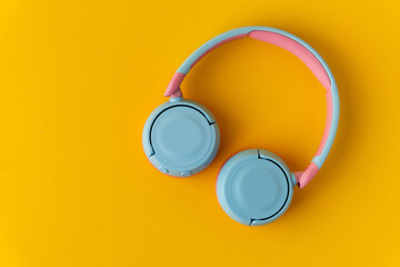 Bright pink and blue wireless headphones on a yellow background. Music and technology concept....