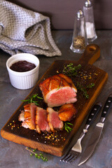 Roast duck breast fillets on wood serving board and cranberry sauce on grey background