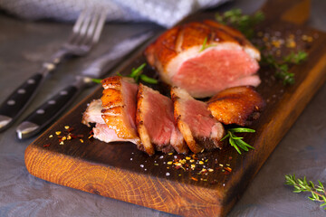 Roast duck breast fillets on wood serving board and cranberry sauce on grey background