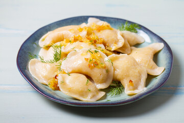 Dumplings with mashed potatoes filling. Varenyky, vareniki, pierogi, pyrohy - dumplings with filling on blue plate on green blue wood background