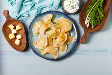 Dumplings with mashed potatoes filling. Varenyky, vareniki, pierogi, pyrohy - dumplings with filling on blue plate on green blue wood background. High angle view