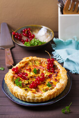 Quiche with chunks of ham, creamy brie and vegetables on blue plate on brown wood background