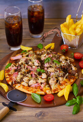 Delicious beef chicken and ham pizza on wood pizza serving plate with chips and fizzy drinks