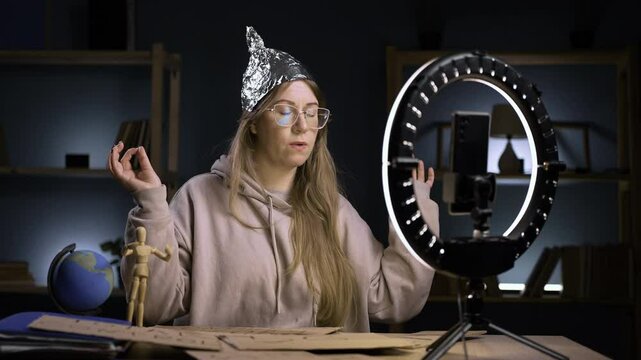 Strange crazy vlogger with cellphone, paranoid woman streaming at home conspiracy theory broadcasting in vlog, meditating calming in yoga pose. blogging and conspiracy theory