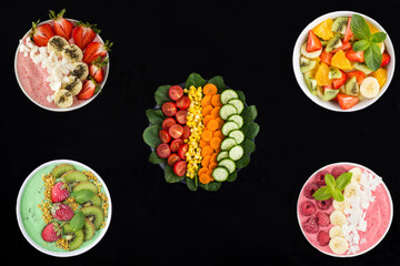 Chopped vegetables, fruit salade and berry smoothie in the bowls on a black background. Top view. Copy space. Healthy food.
