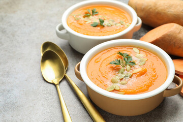 Delicious sweet potato soup with pumpkin seeds in bowls and fresh vegetables on grey textured table, closeup
