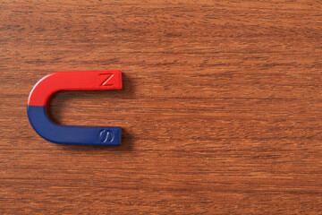 One horseshoe magnet on wooden background, top view. Space for text