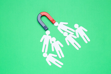 Magnet attracting paper human figures on green background, flat lay